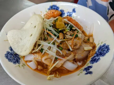 A bowl of mì Quảng noodles with shrimp, pork and a rice cracker